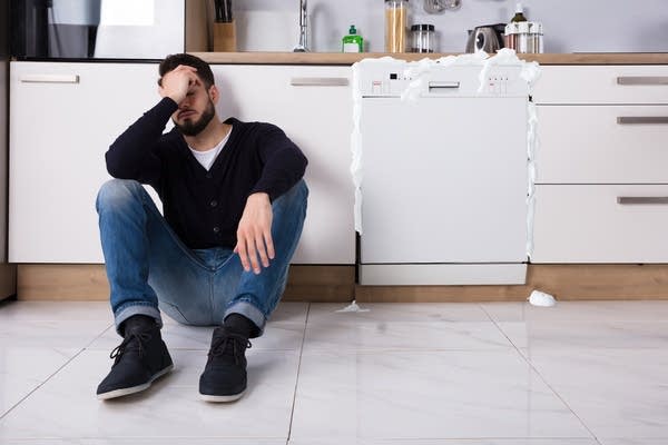 White man w/ beard sits sadly next to his broken dishwasher