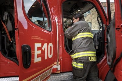 A firefighter puts gear in the cab of a fire engine.
