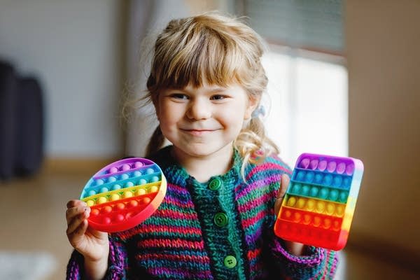 Little blonde preschool girl playing with new trend sensory toy - rainbow pop it. Antistress toy for children and adult. Colorful toy simple dimple. Squishy soft bubble toys rainbow color. Happy child.