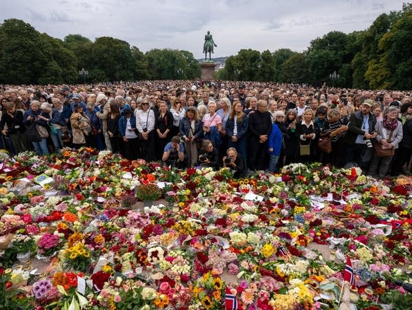 Mourners gather in front of a display of flowers