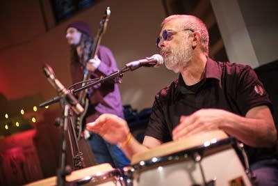 A musician plays bongos and sings onstage
