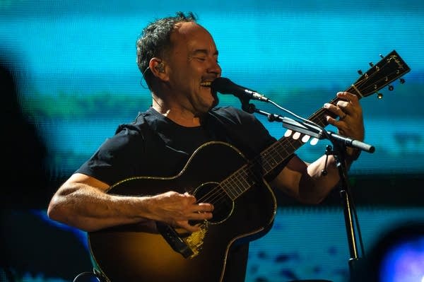 A musician sings and plays acoustic guitar on a large outdoor stage