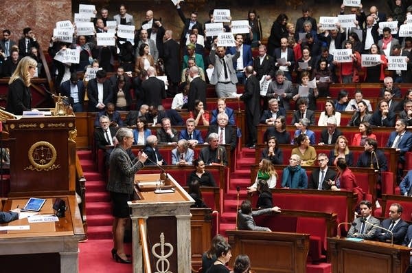 Members of Parliament of left-wing coalition NUPES (New People's Ecologic and Social Union) hold placards during the speech of France's Prime Minister Elisabeth Borne (C), as she confirms to force through pension law without parliament vote during a session on the government's pension reform at the lower house National Assembly, in Paris on March 16, 2023. - French President forced through pension law without parliament vote, after he  won approval from the upper house Senate for his reform of the pension system, which has sparked massive protests and strikes since the start of the year. (Photo by Alain JOCARD / AFP) (Photo by ALAIN JOCARD/AFP via Getty Images)