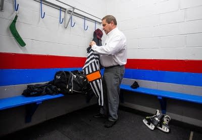 A man wearing a button down shirt and slacks holds a referee uniform. 