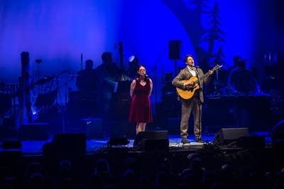 a vocalist and guitarist singing on stage with a backing band
