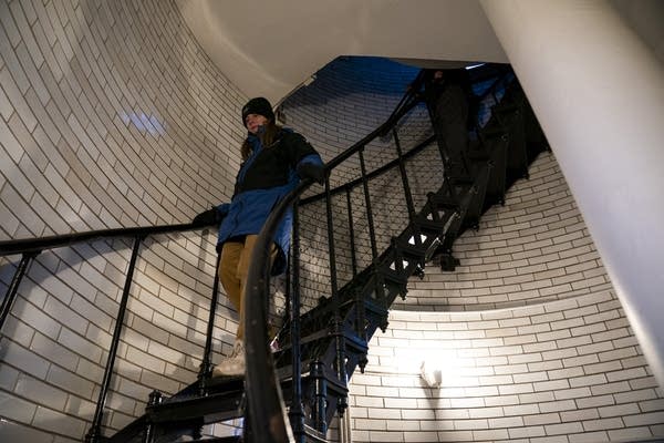 A woman walks down a spiral staircase inside a lighthouse.