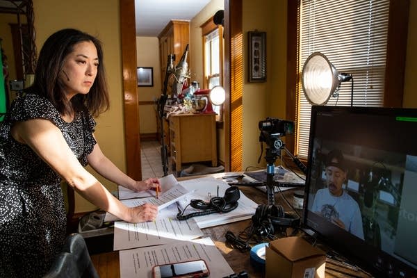 A woman leans on a table covered in papers.