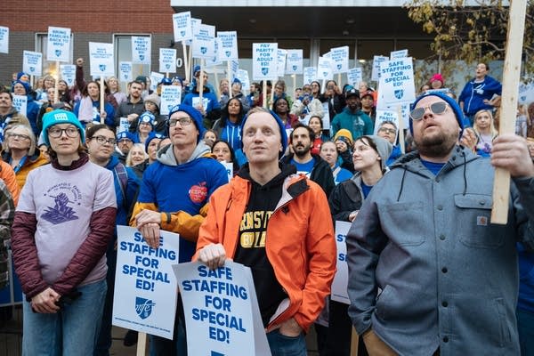 A crowd of demonstrators hold white and blue picket signs.