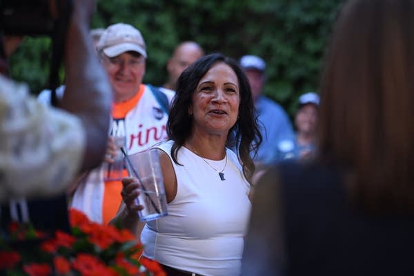 A politician holds a glass while speaking to a crowd of supporters.