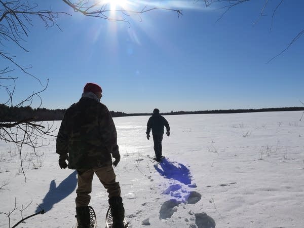 Two people snowshoe in a snow-covered field.