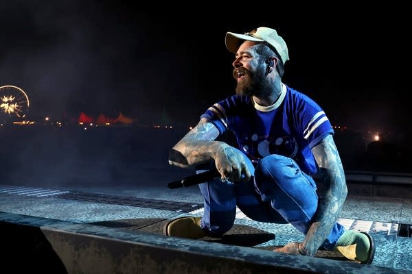 A man squats and smiles at the audience while performing onstage