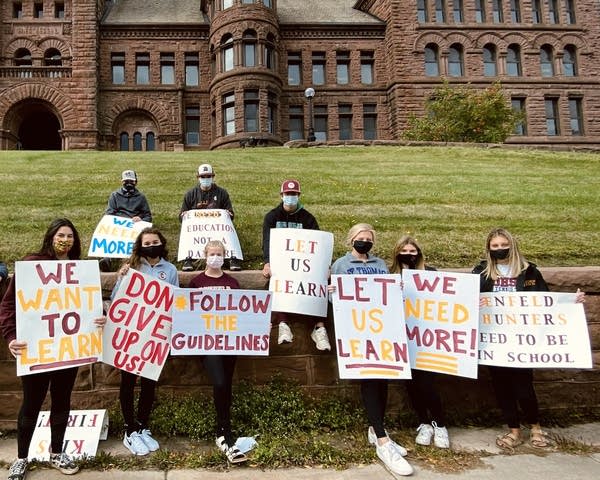 A group of teens hold signs in front of a brick building. 