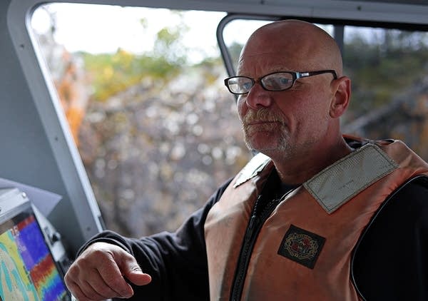 A man in a faded orange life jacket sits in a boat's cockpit.