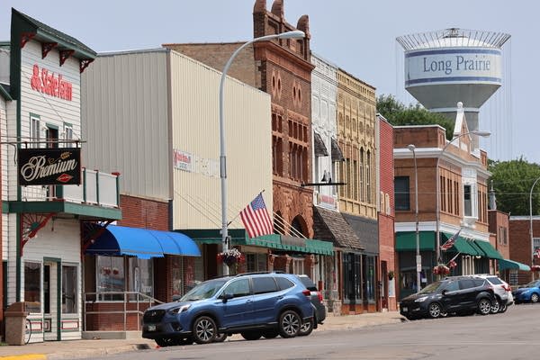 A shot of downtown Long Prairie, with storefronts and cars seen in the foreground and a water tower in the background.