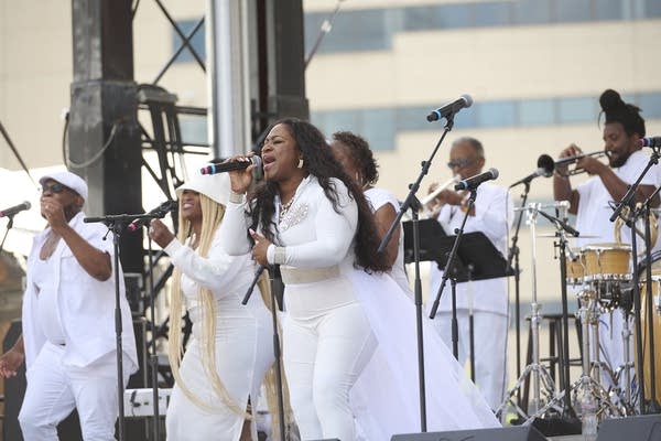 A woman sings with a large ensemble performing on an outdoor stage