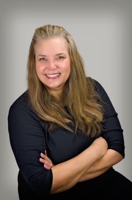 A woman with her arms folded smiles into the camera