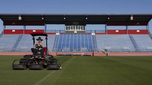 A worker mows lawn at a sports complex.