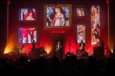 Band performing on stage with multiple paintings projected behind