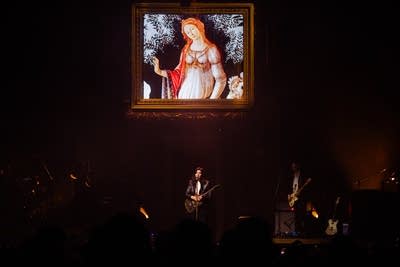 Band performing on stage with painting projected behind