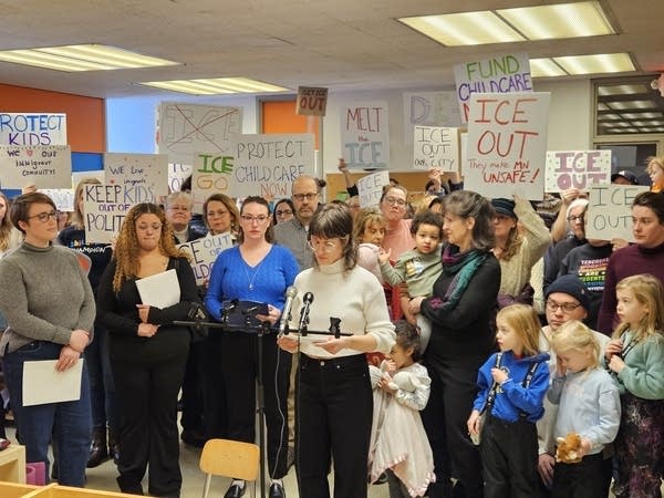 Woman speaks into microphone with crowd behind her