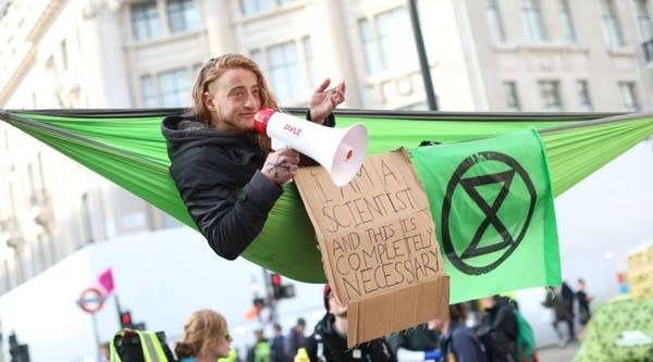 A climate change activist in a hammock occupying Oxford Circus in the busy shopping district of central London on April 18, 2019 uses a megaphone on the fourth day of an environmental protest by the Extinction Rebellion group. - Nearly 300 people have been arrested in ongoing climate change protests in London that brought parts of the British capital to a standstill, police said on April 17.