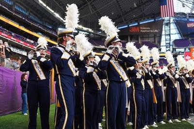 A marching band performs on the field of a football stadium.