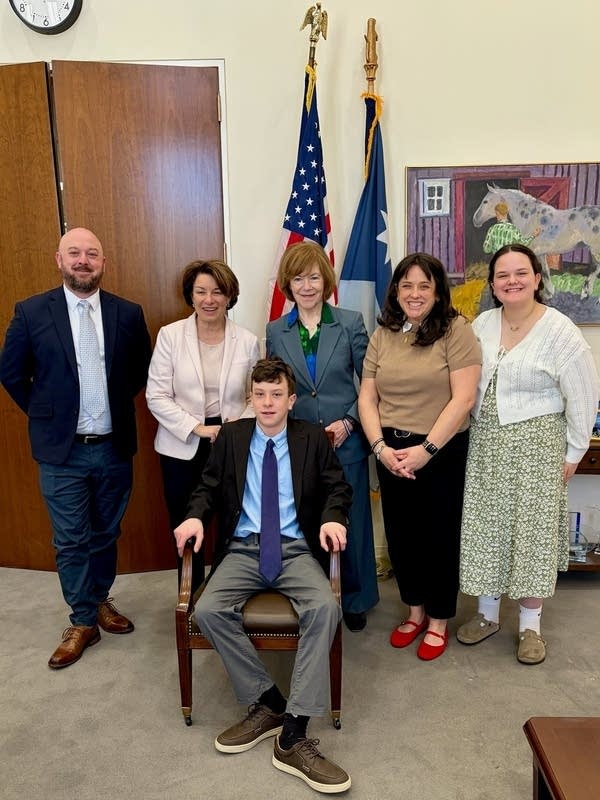 Six people smile with U.S. and Minnesota flags behind them
