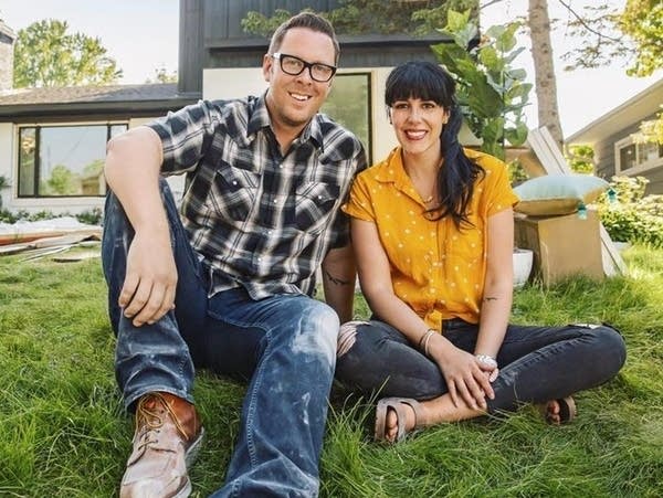 A man and woman sit in a yard in front of a house.