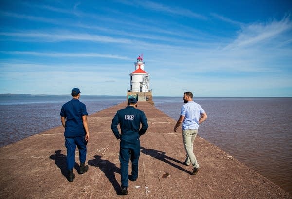 Three people walk to a lighthouse.