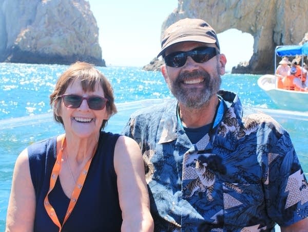 Two people smile by the ocean with cliffs in the background