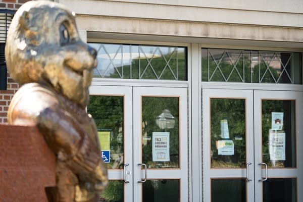 A gold statue of a gopher stands in front of doors with signs.