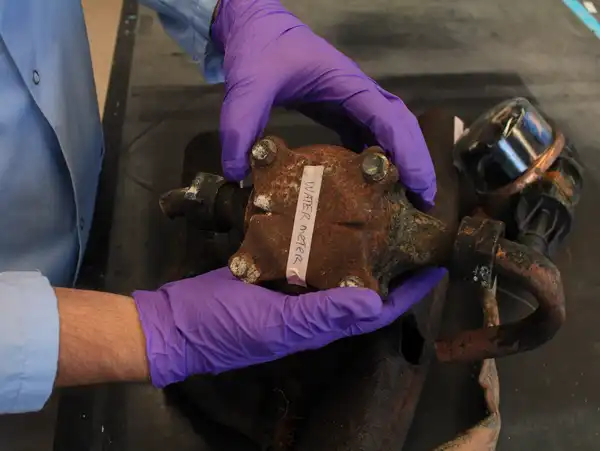 A pair of hands wearing purple gloves holds a rusty piece of metal.