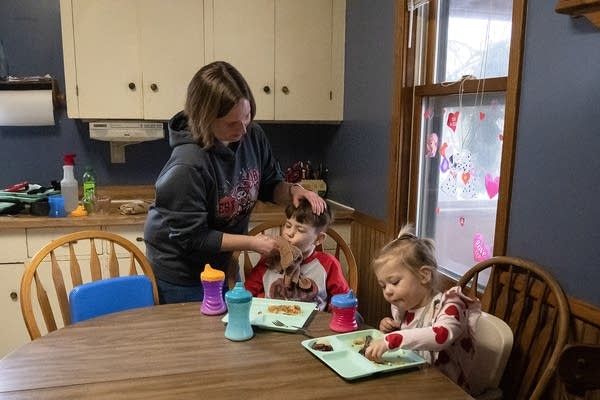 A woman wipes the face of a child that is eating a meal.