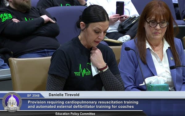 A woman holds a tissue to her chest while testifying in front of a government committee.