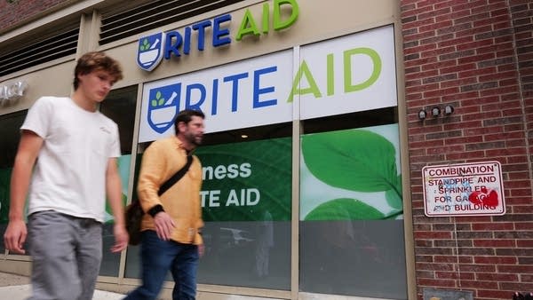 Two people walk past a Rite Aid store on a Brooklyn street