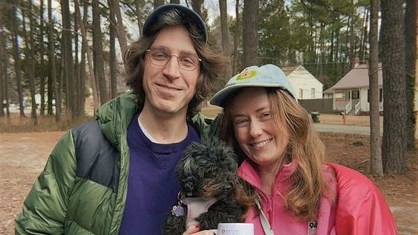 A couple poses with a small black dog between them.
