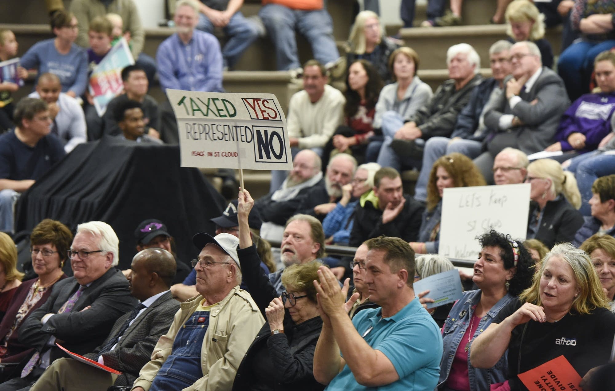 People hold signs during a St. Cloud City Council discussion on refugees.