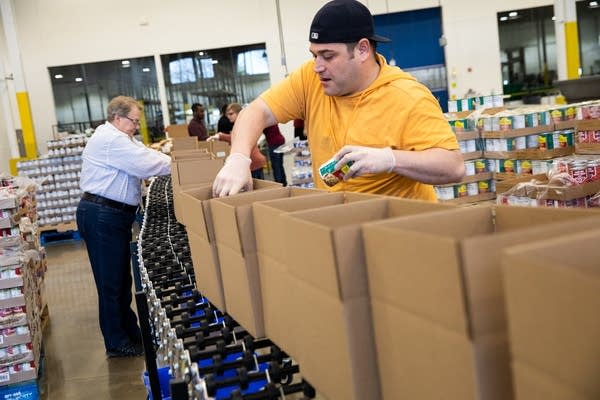 A man puts cans of beans into cardboard boxes.