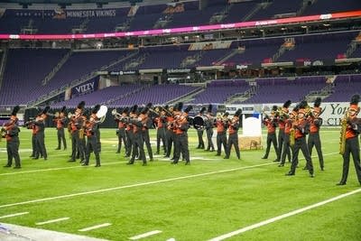 A marching band performs on the field of a football stadium.