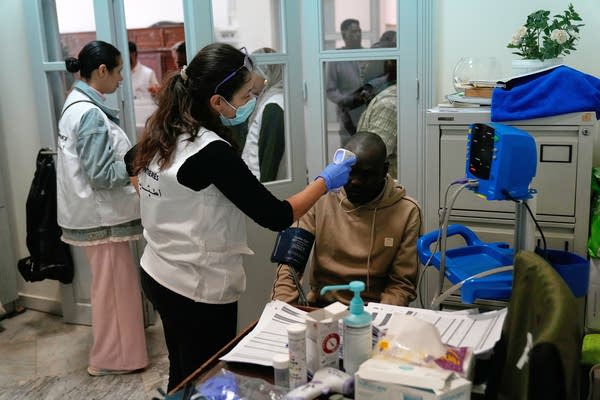 A doctor checks a patient's forehead in a busy clinic.
