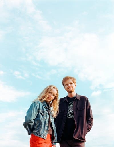 Two people in lightweight jackets stand beneath a wispy-clouded sky 
