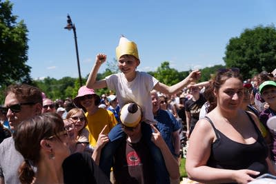 A child wears a pencil shaped hat while sitting on an adult's shoulders
