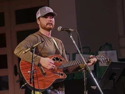 A man holds a guitar while standing near a microphone.