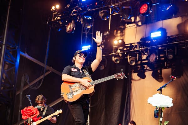 A musician with a guitar greets the audience from stage