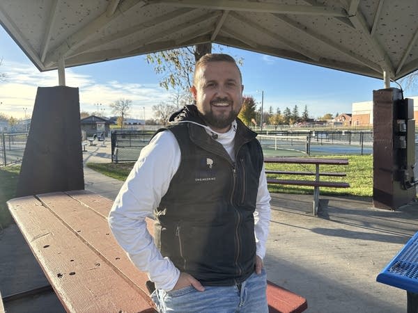 A man in a black vest poses for a photo at a park.