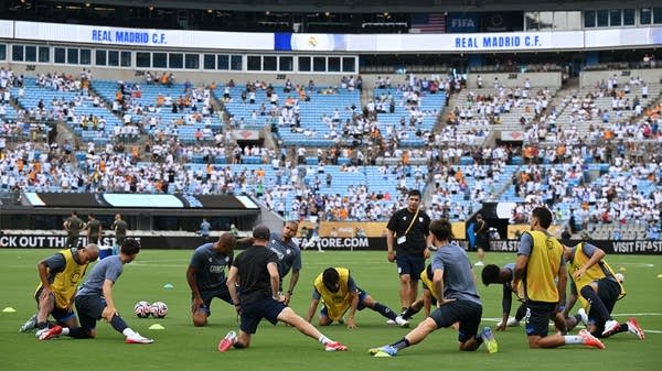 Soccer players warm up in front of a sparsely filled stadium.