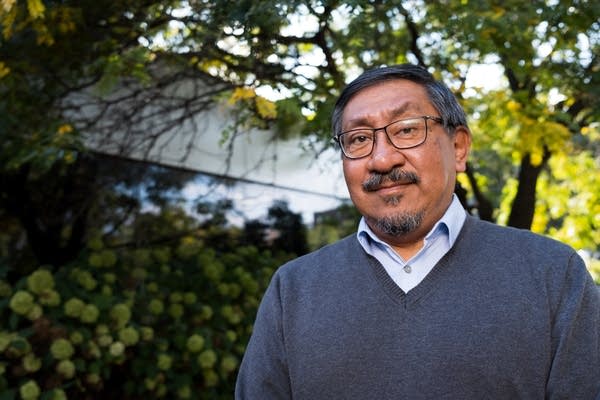 A man stands in front of foliage.