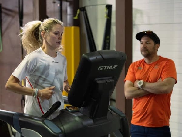 Jessie Diggins runs on a treadmill with a coach watching nearby.