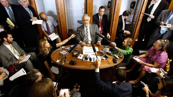A man surrounded by microphones and reporters.