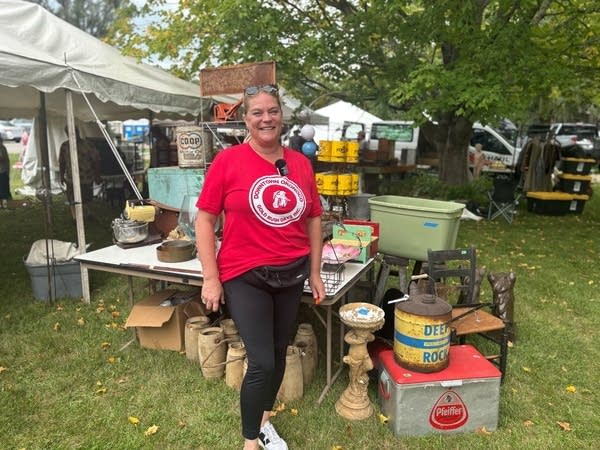 A woman in a red shirt poses for a photo in front of a table full of goods.